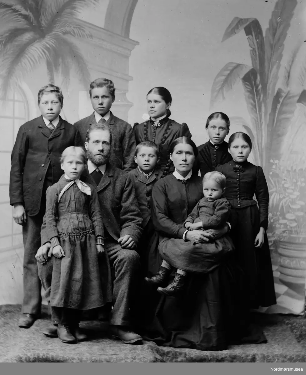 Familie, atelier. Familiegruppe av familien til Jon Ols. Flatvad og kona Marit Eriksdtr. f. Gjøra med 8 born. Personene framme fra v.: Anne, far Jon, Eyvind, mor Marit med Ingrid på fanget og Oline, bak fra v.: Ole, Erik, Marit g. Wennevold og Kristine. Jon var en leder i bygda og han er omtalt slik i Sunndalsboka (I. Seljedal b. 2 s. 255): "Han var et ypperlig hode, en slagferdig mann, atskillig benyttet til kommunale gjøremål. Han var ordfører i Sunndal 1872-85 og 1890-91".