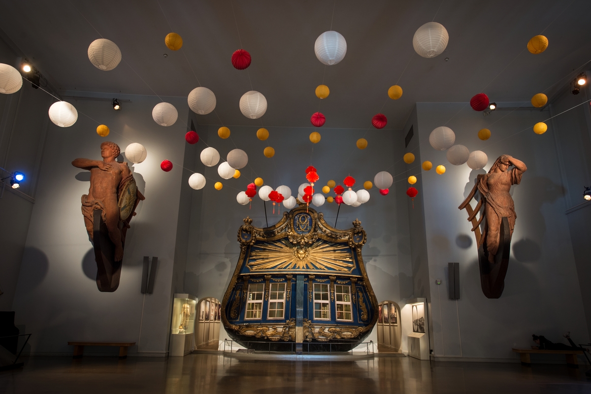 Papperslampor i Minneshallen inför invigningen av utställningen "Resenärerna" på Sjöhistoriska museet. I bakgrunden akterspegeln från den kungliga lustjakten Amphion.