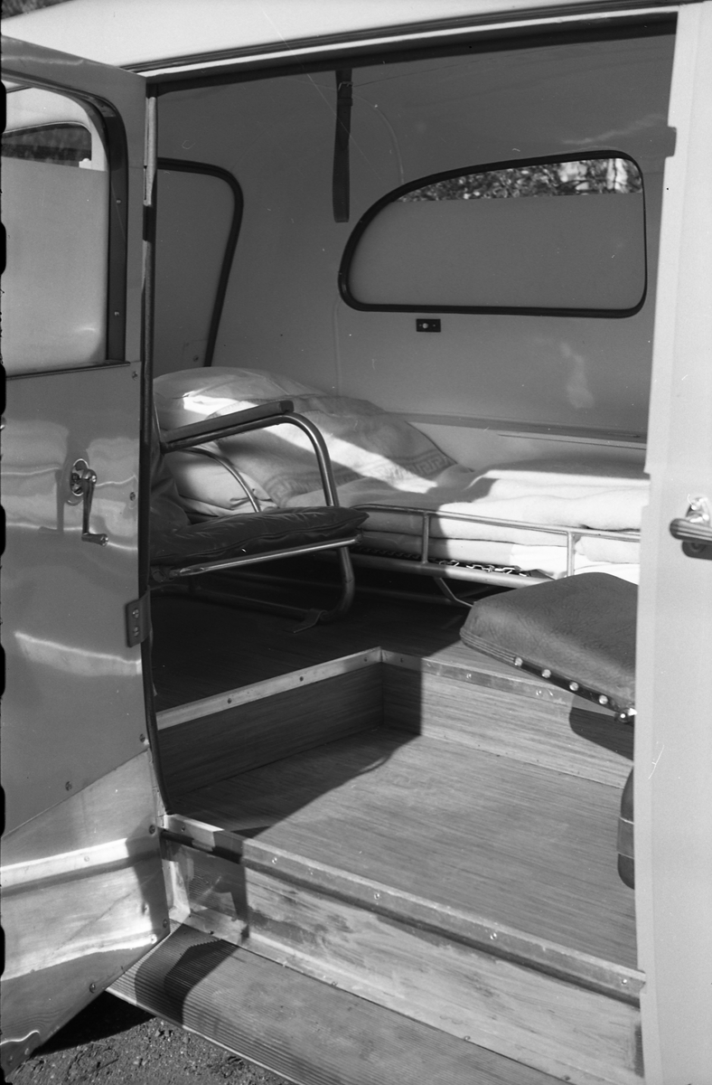 Ambulanse, muligens den første anskaffet av Østre Toten Sanitetsforening. Serie på 12 bilder fra september 1948. Kvinnen på bilde nr. åtte er Gjertrud Solem som trolig er sanitetsforeningens representant, mens mannen på bilde nr. sju, og som nok er sjåføren, er Anders Skolby fra Kapp. Han ble senere sjåfør for kronsprins Olav på Skaugum, og etter det privatsjåfør for Anders Jahre .