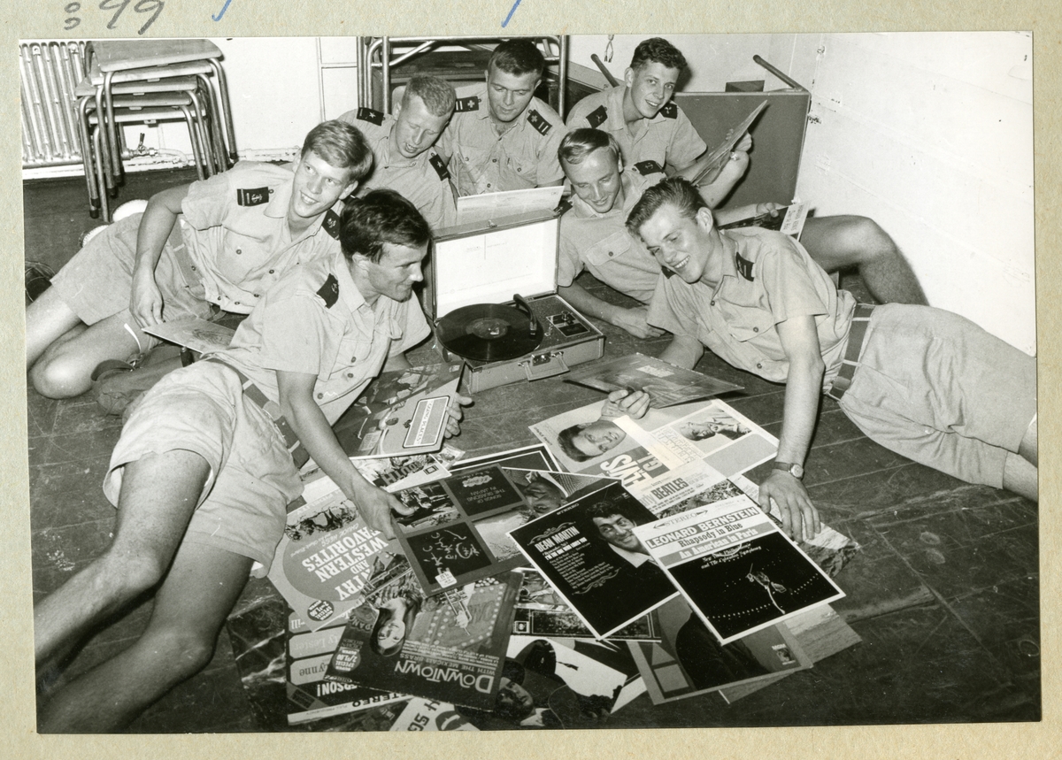 Bilden föreställer sju uniformsklädda besättningsmän ombord på minfartyget Älvsnabben, vilka ligger på golvet i spisarhörnan med en hög vinylskivor och lyssnar på musik. Vinylskivornas ägare, matrosen Unsgaard, med sknr 347, blev sedermera präst i Svenska Kyrkan; kyrkoherde i Bromma församling Stockholm.