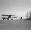 Varmkörning av motor på flygplan Gloster Gladiator inför start från F 19 i Veitsiluoto, Svenska frivilligkåren i Finland. Militärer i arbete. Ett pappersbruk syns i bakgrunden.