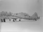 Sovjetiskt flygplan Iljushin DB-3 står på ett fält under finska vinterkriget, 1940. Människor i rörelse runtomkring. Vy bakifrån. Bild från F 19, Svenska frivilligkåren i Finland.