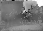 Utetagning vy 1920. Repro. Gatan. En samling herrar varav en med en cykel.