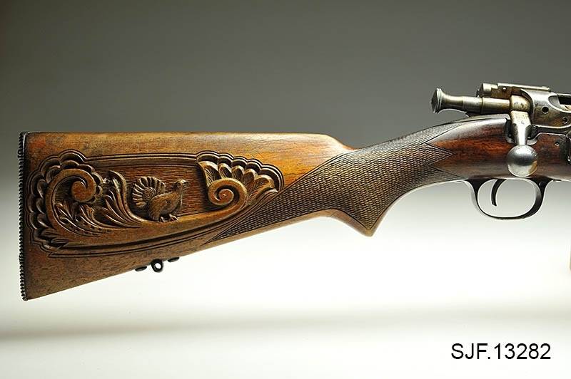 Krag-Jørgensen rifle med kaliber 6, 5 x 55. Geværet har pistolgrep. Magasinkapasitet på 5 patroner. Kolben er brunbeiset / oljet. Skjeftet er dekorert med forseggjorte utskjæringer.  Kolbekappen av stål har innfelt et lokk. Om man åpner lokkket kommer man til et "oppbevaringsrom" i kolben. Treverket som omslutter undersiden av geværløpet har noen sprekkdannelser.  Geværet er utstyrt med høydejusterbart skur og sidejusterbart korn. 