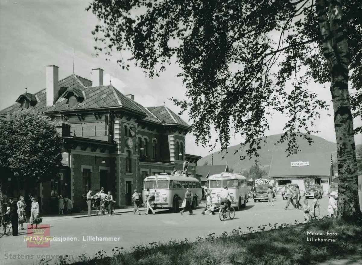Bilde fra Lillehammer jernbanestasjon en sommerdag 1951-1956, som viser både gående, syklende og reisende til og fra stasjonen. Reisebyrået er til høyre på bildet. Skiltet på bussen til venstre viser Dalseter og Skåbu, hvor buss-sjåføren står på taket og fester bagasjen til passasjerer. Bussen til høyre er skiltet til Gausdal. Bilen ved siden av bussen er en Ford og bilen nr. 3 fra venstre er en Plymouth. 

De to bilene er 1946-47 Ford og 1951-52 Plymouth.
(Opplysninger til kjøretøyene fra Asbjørn Rolseth).