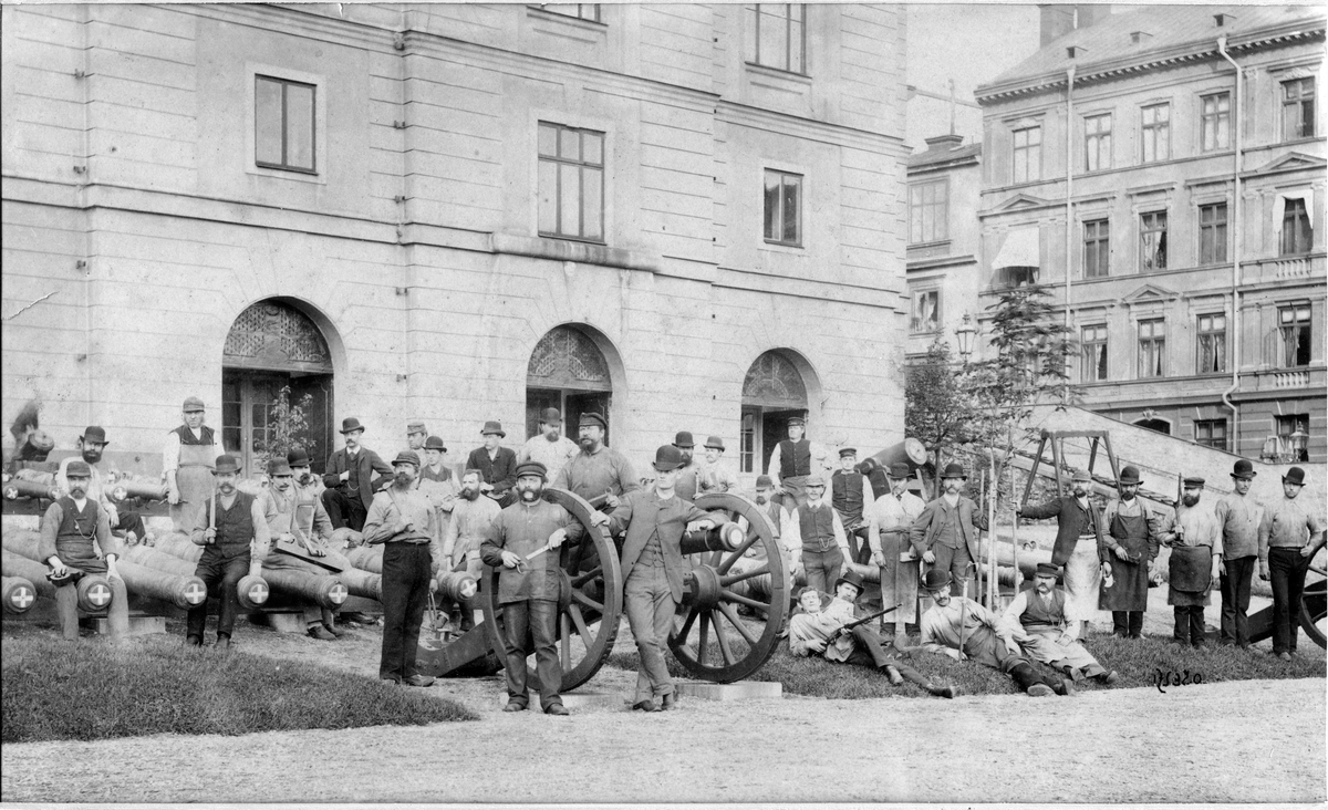 Grupp av hantverkare utanför tyghusets (Armémuseum) östra del vid kanonerna.