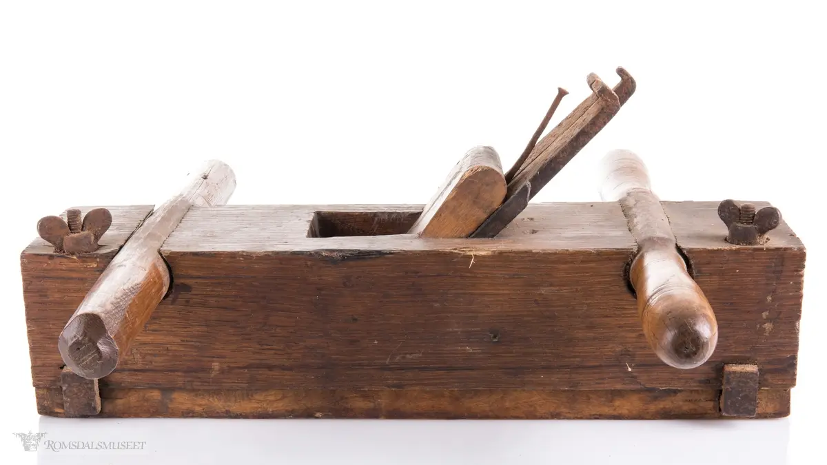 Rektangulær okshøvel med jern og kile. Jernet kan reguleres med skrumekanisme. Et dreid og et skåret håndtak er felt ned i avrundede spor foran og bak. Spor for høvling av fjær i sålen og regulerbare styringslister på hver side av sporet.