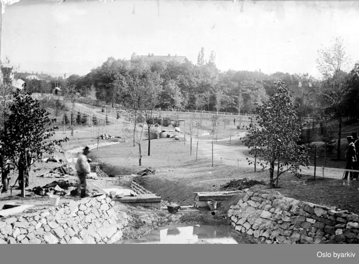 Anleggsarbeide - anlegg av bekk på St. Hanshaugen. På høyden i bakgrunnen , taket på våningshuset på "Høien" - i dag Schwensensgt. 11. Til høyre skimtes to hvite piper på taket til våningshuset på løkken Frydenlund (Christensens løkke), revet 1893. Bak det lille gjerdet midt i bildet går Ullevålsveien i dag.