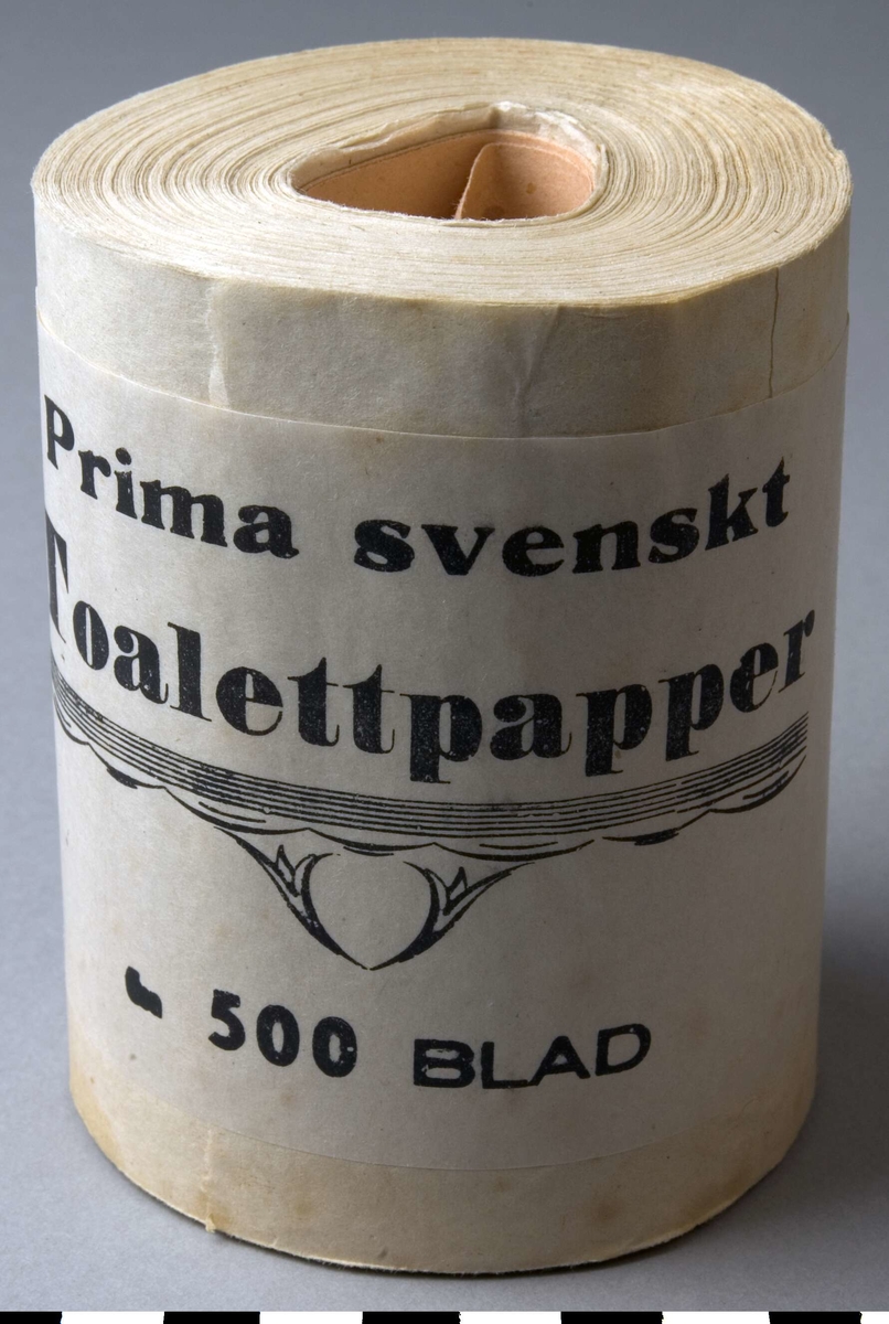 Förpackning, toalettpappersrulle, 5 st, A-E.
Papprulle i mitten, med pårullat toalettpapper. Ytterst ett pappersomslag med bård och text i svart. Dekoren är ett band med bågar i underkanten och två blommor under.
Text: Prima Svenskt Toalettpapper. 500 BLAD.