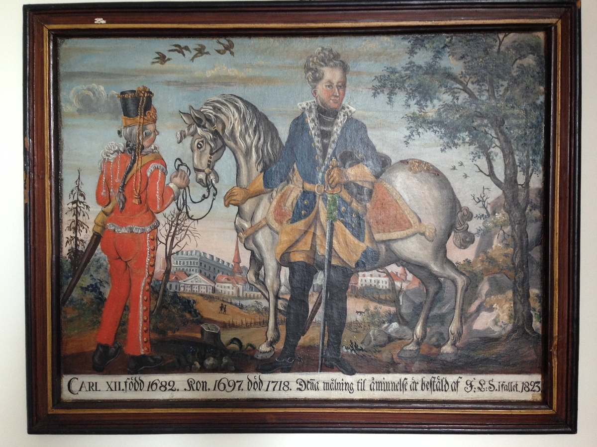Oljemålning på väv, av Hans Wikström. Motiv: Karl XII stående framför vit häst, vilken hålles av soldat i röd uniform. I bakgrunden landskap med "stenstad" i fonden. Textfält nedtill: "CARL XII. född 1682. Kon. 1697. död 1718. Dena målning til åminnelse är bestäld af F:L:S. i fallet 1823". Även blyertssiffror i fältet. Monterad/spänd direkt i prydnadsramen med trästift. Ramen brunådrad med bårder i svart och guld.