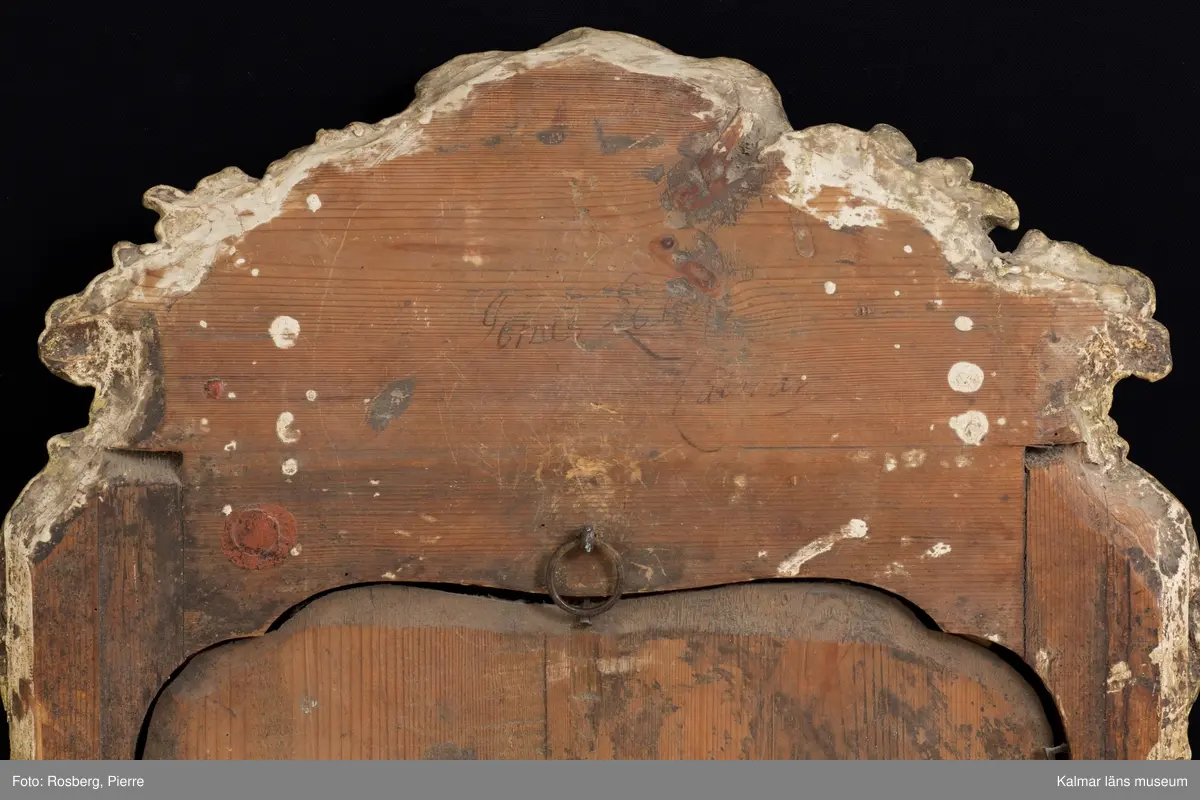 KLM 14346. Spegel, väggspegel. Förgylld ram av trä med snidade rokokoornament. Spegelglaset i två delar, facetterat, det övre spräckt. På baksidan Kalmar hallstämpel (ej den vanliga) samt otydlig signatur, troligen: Jonas Löw Kalmar. Rokoko.