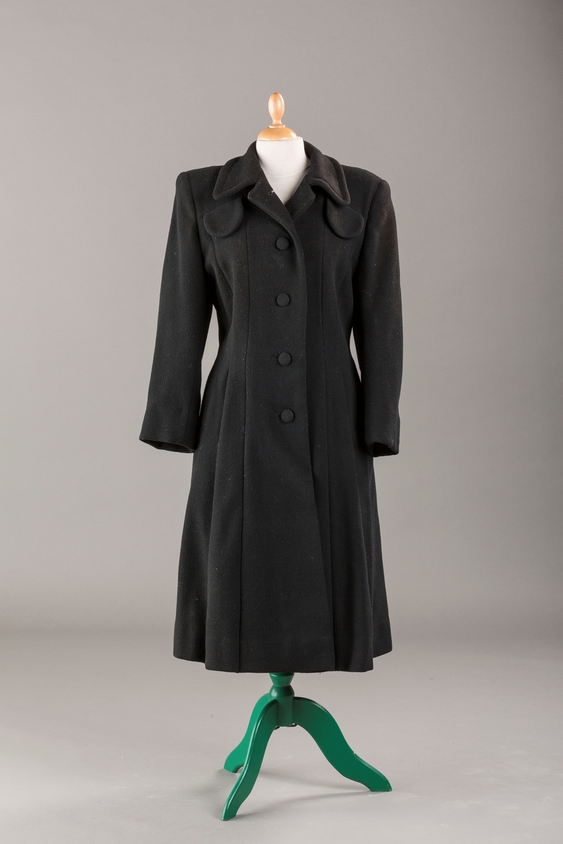 Innsvinget liv, pynteklaffer ved brystet foran. 
Stikklommer foran.
Skulderputer
Fire trukne knapper
Avrundet krage