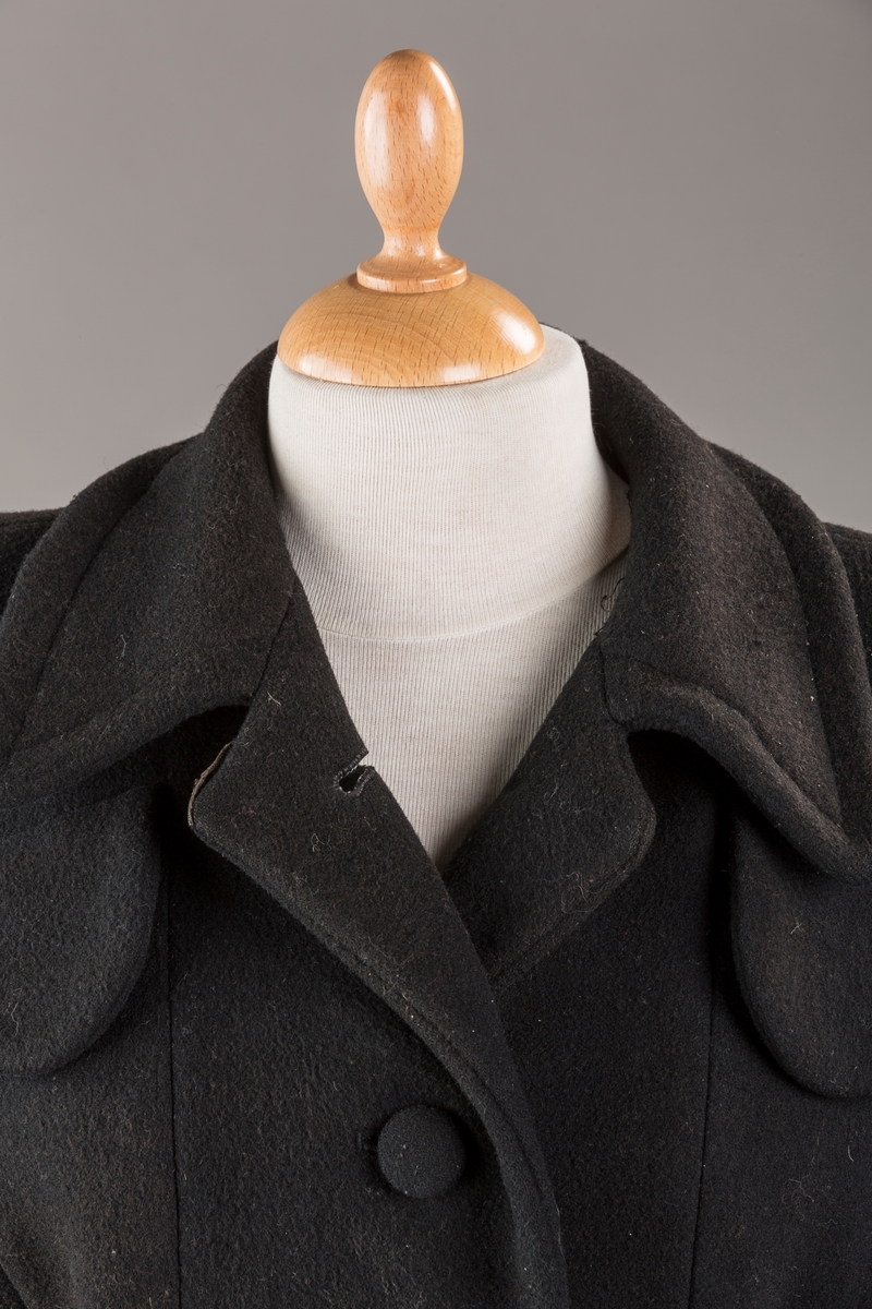 Innsvinget liv, pynteklaffer ved brystet foran. 
Stikklommer foran.
Skulderputer
Fire trukne knapper
Avrundet krage