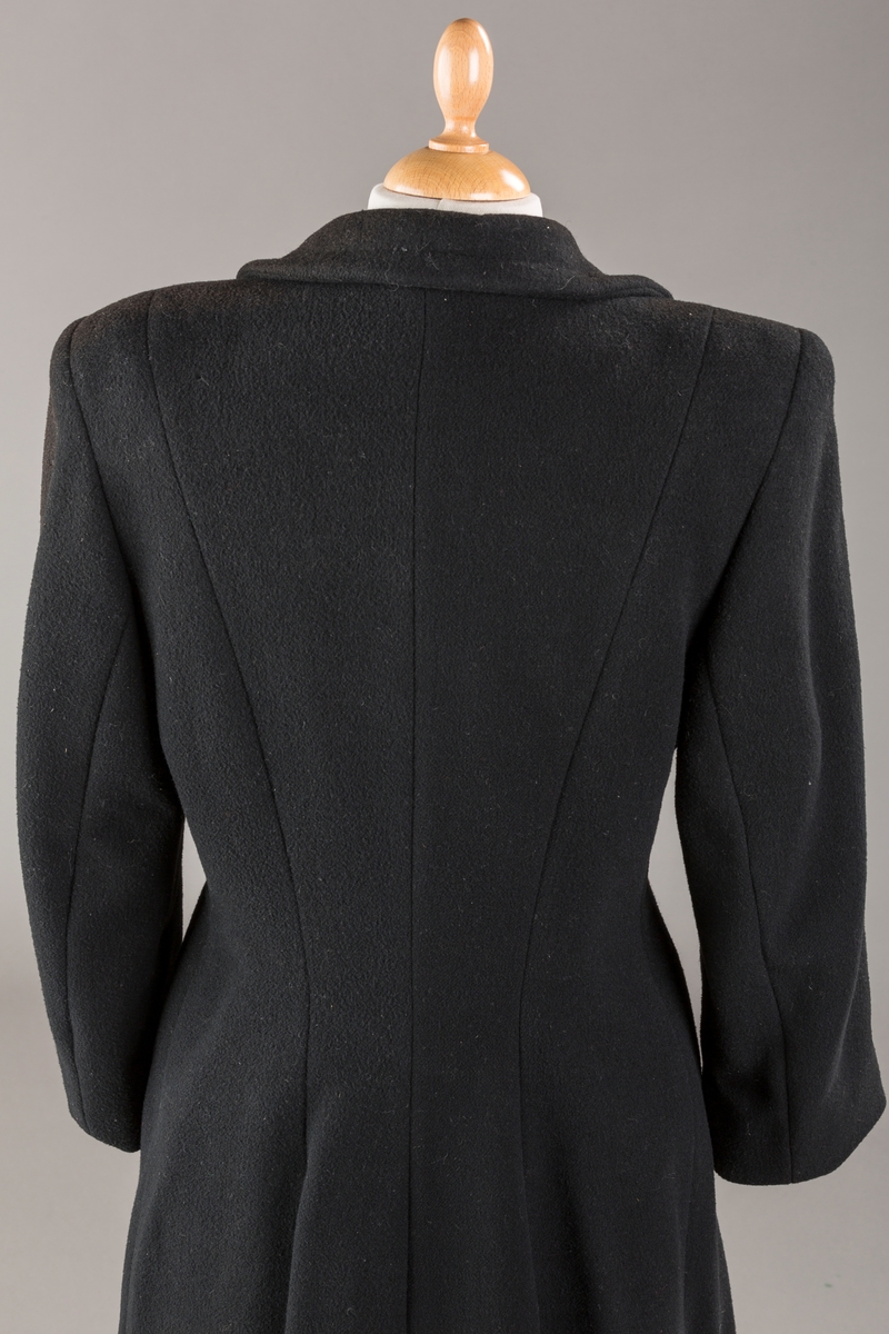 Innsvinget liv, pynteklaffer ved brystet foran. 
Stikklommer foran.
Skulderputer
Fire trukne knapper
Avrundet krage