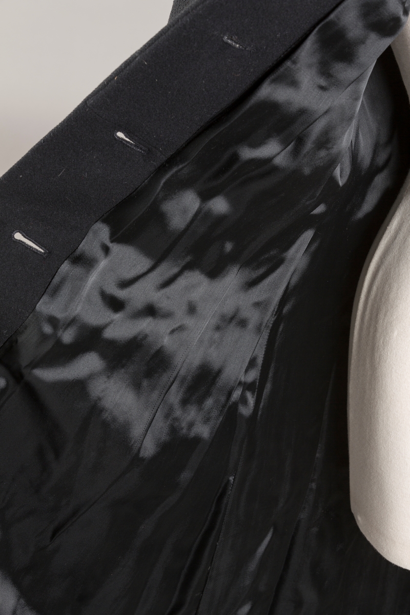 Innsvinget liv, pynteklaffer ved brystet foran. 
Stikklommer foran.
Skulderputer
Fire trukne knapper
Avrundet krage