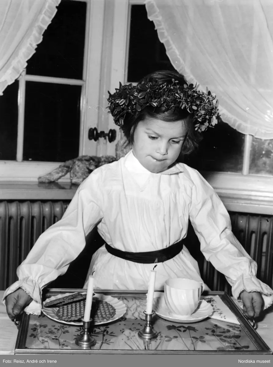 Luciafirande. Liten flicka klädd som tärna lyfter en bricka med kaffekoppar och våfflor
