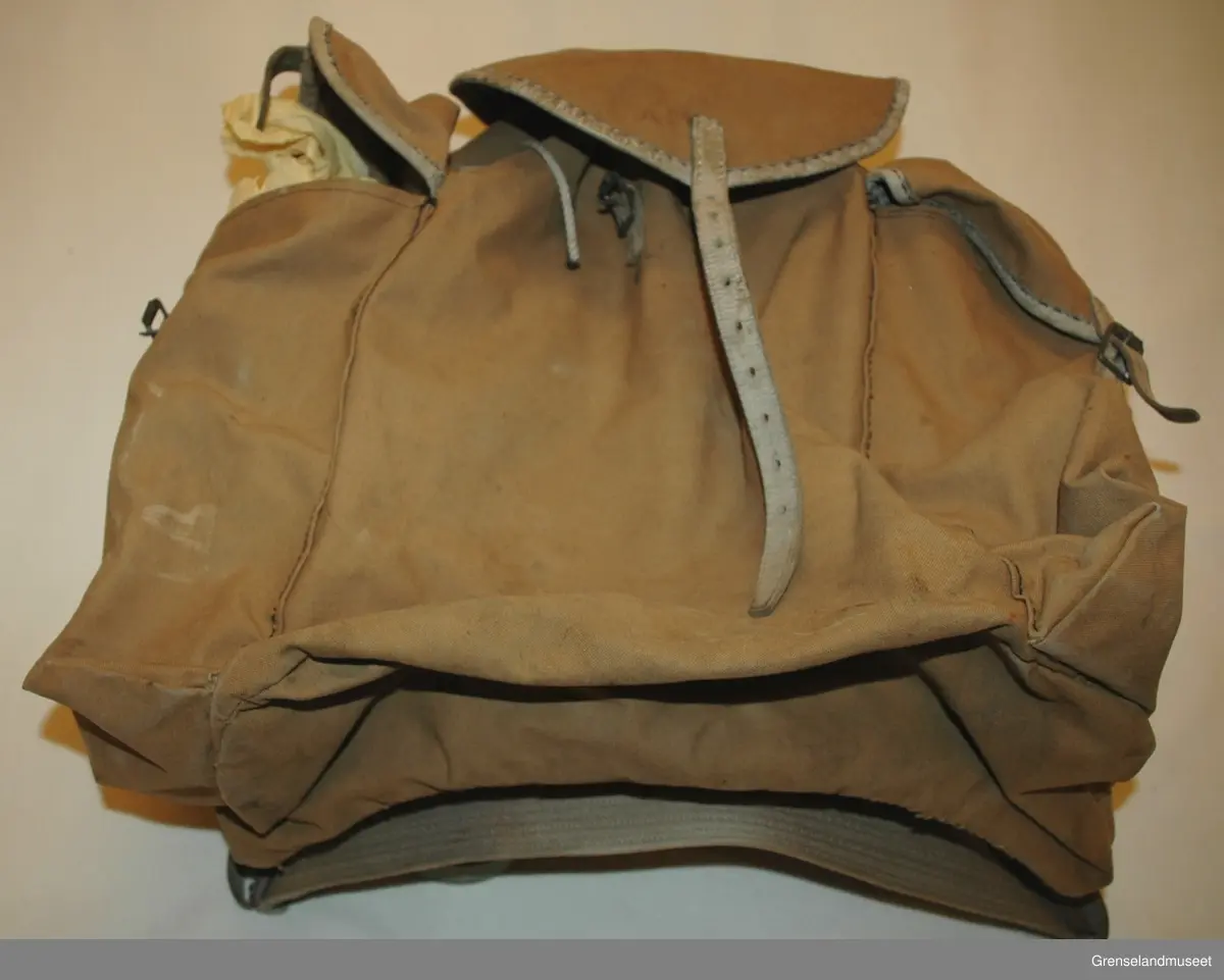 beige (eller falmet grå?) seilduk. Lærremmer med spenner. Sydde hull for snor i toppen.