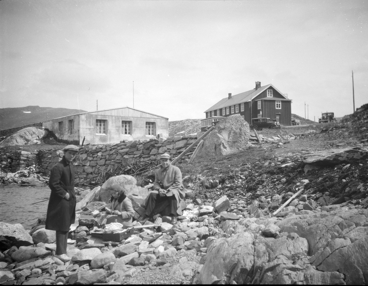 Stort trehus og murbygning på  fjellet med 3 mennesker i forgrunn. Muligens ved Tyin.