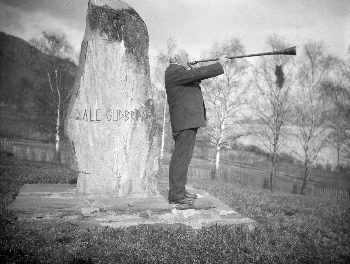 Professor Fredrik Pasche blåser i lur ved minnestein over Dale-Gudbrand og Olav Haraldsson ved Gudbrandsdalens Folhehøgskule, Hundorp. Ble satt opp sommeren 1928.