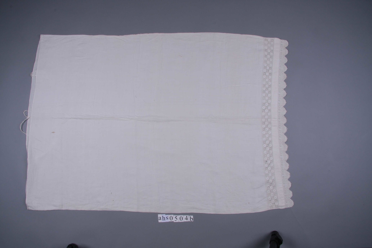 Hvit linlerret åpne i den ene kortsiden med smal fall og knytebånd. I motsatt ende en meget fin, tunget knipling med palmett-mønster. Tungespissene er sydd sammen med en liten stolpe. Innenfor kniplingen en 4 cm. bred meget fin reticella-bord mellom to rader austmannarenning.