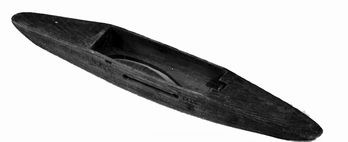 Avlang vevskyttel av tre med uthuling på midten, der hullet i bunnen er formet som en ranke.