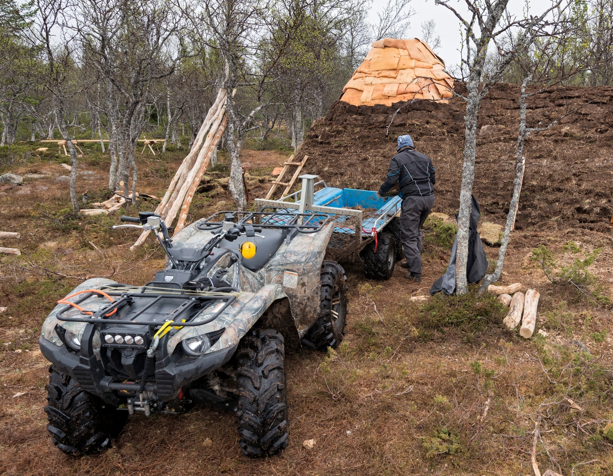 Bilde tatt i forbindelse med legging av torv på gamme. Fra gjenreisingen av Daniel Mortenssons vinterboplass ved Kjerran, Valdalsfjellet, Engerdal. Mats Mortensson bærer torv han transportert med ATV. Rekonstuksjon av Daniel Mortensons vinterboplass. Rekonstruksjon av samisk boplass. I følge Jonas Danielsen ble Daniel Mortensons vintergammen oppført i løpet av perioden 1900— 1902. Svahken Sijte hadde et ønske om å gjenreise en vintergamme, daelvie-gáetie, i nærheten av gammetuften, og stedet som ble valgt til formålet ligger ca. 50 meter nord for den gamme tufta. Gamma sto ferdig i begynnelsen av juni 2017, og åpningen inngikk i jubileumsmarkeringen for samenes første landsmøte i 1917, Tråante 2017. Samisk vinterboplass. Samisk kultur og historie. Daniel Mortenson. Daniel Mortensson.