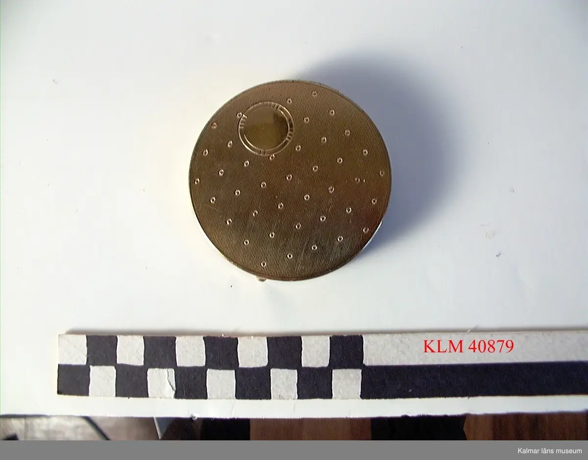 KLM 40879 Puderdosa, metall. Rund, av gul metall, ovansidan med dekor av en större och många små cirklar. Med spegel inuti.