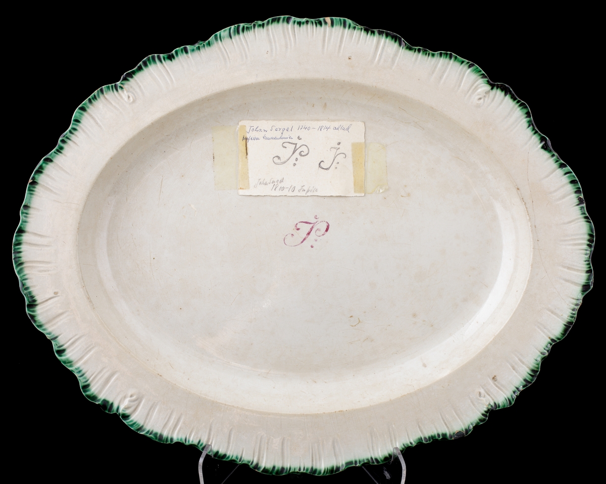 Stekfat av flintgods.
Oval modell. Vitglaserat med grön s.k. "feather edge"-kant. På fatets spegel monogram i vinrött: "JS". 
På fatet fäst en lapp med text: "Johan Sergel (1740-1814), adlad professor vid Konstakademin, Johan Sergel 1800-10, Inköp".