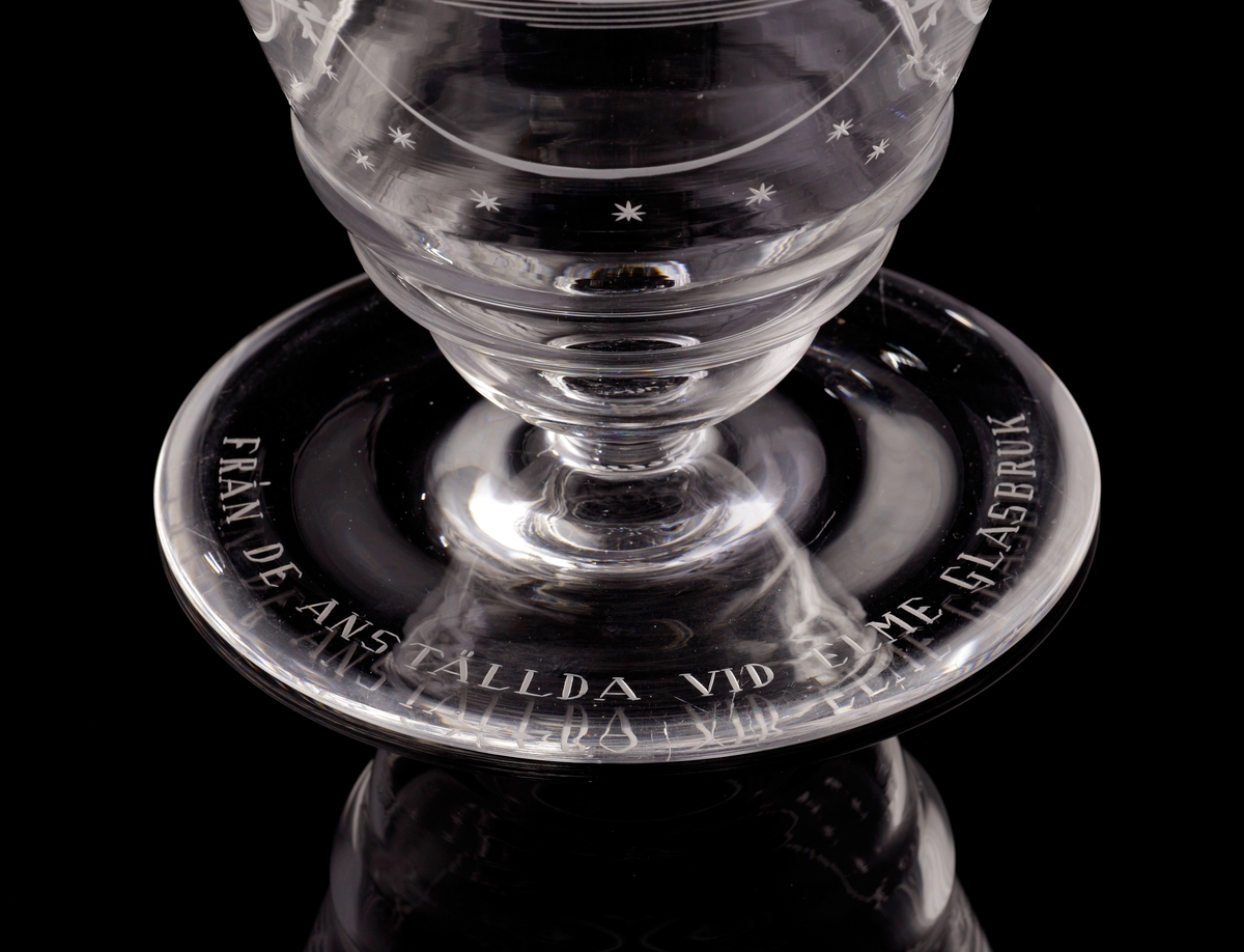 Pokal med lock.
Pokalen är balusterformad med en frikostig diameter på dess övre del.
Pokalens undre del smalnar av kraftigt och avslutas med en relativt stor fot.
Locket presenteras i olika etager och avslutas med en hög knopp.
På pokalen graverade girlanger och stjärnor, samt ett monogram och en bild på Elme glasbruk.
På locket graverad girlang och stjärnor, och på knoppen graverat "Elme".