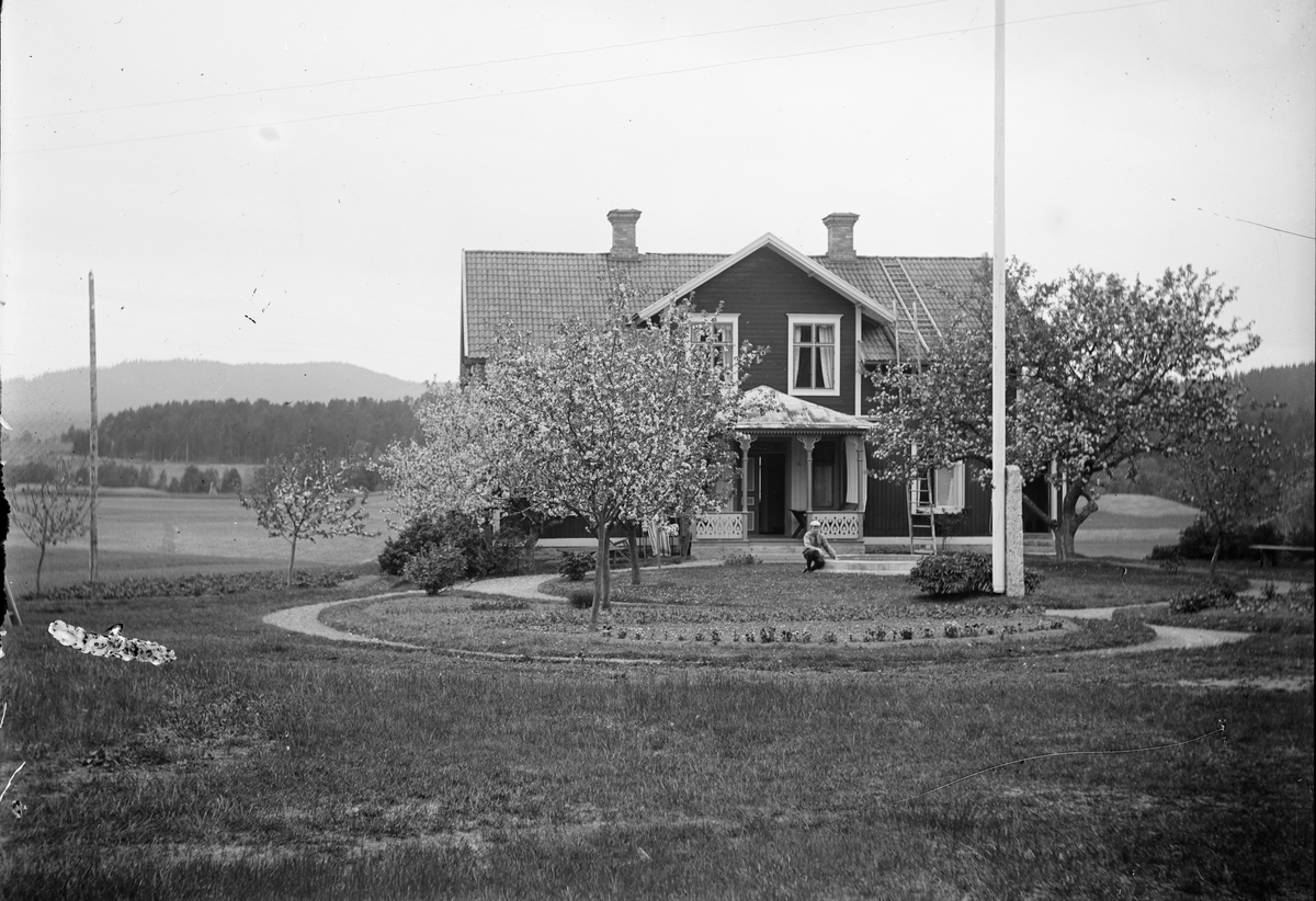 Sannolikt någon av Ruben och Christiane Liljefors söner, sitter i trädgård framför bostadshus, sannolikt Svensgården i Dalarna