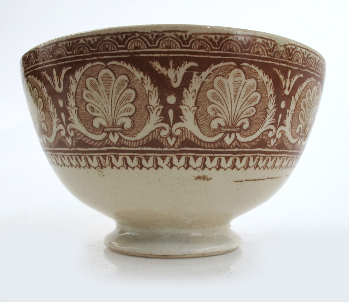 Bolle, stentøy, Buede sider, innsvunget fotring; trykt mønster i  brunt: Innv. og utv. bred ornamental bord m. skjell og "Garrya Eliptica" i bunnen lignende dekor, her er skjellene plassert i korsform i et rundt felt. Tilst. juli 1961: Krakellert.