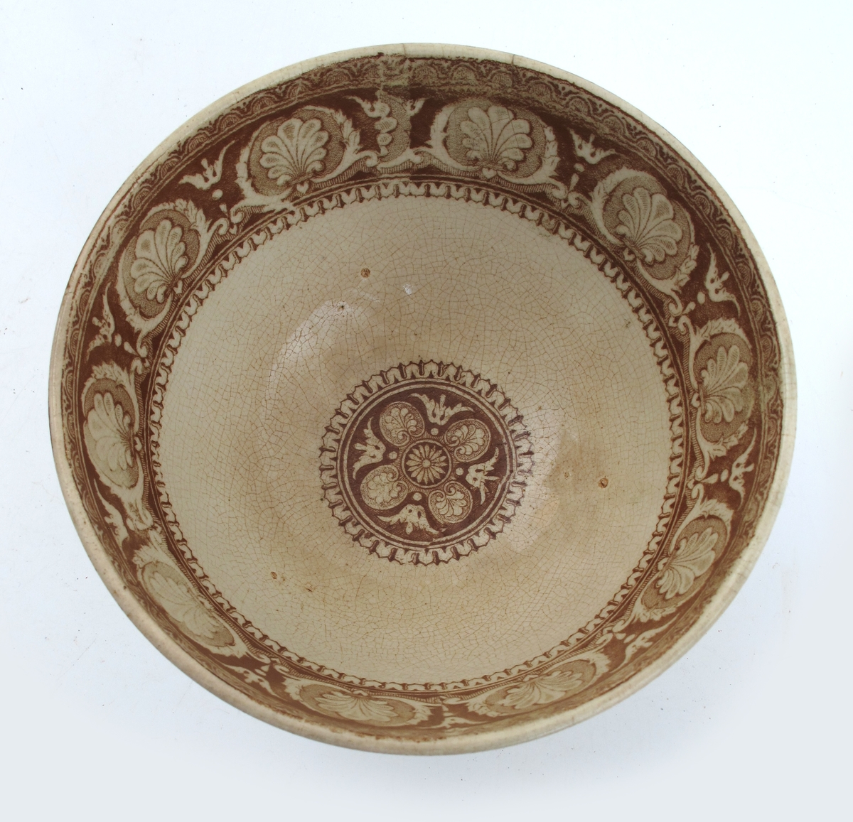 Bolle, stentøy, Buede sider, innsvunget fotring; trykt mønster i  brunt: Innv. og utv. bred ornamental bord m. skjell og "Garrya Eliptica" i bunnen lignende dekor, her er skjellene plassert i korsform i et rundt felt. Tilst. juli 1961: Krakellert.