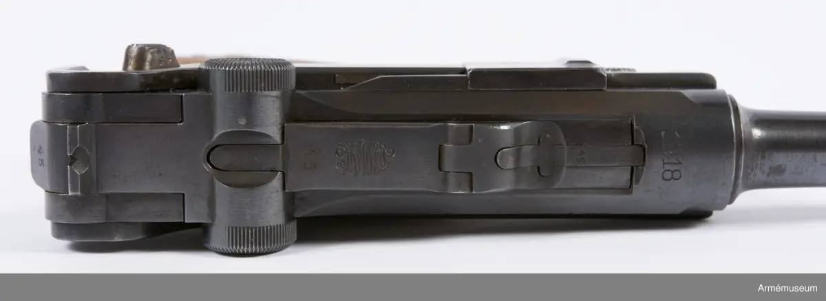 Kolvsidor av trä.
Hölster och extramagasin saknas.
Stämpel på ovansida från Deutsche Waffen- und Munitionsfabriken (DWM), Berlin. Där tillverkades de allra flesta av Parabellumpistolerna mellan 1900-1930.