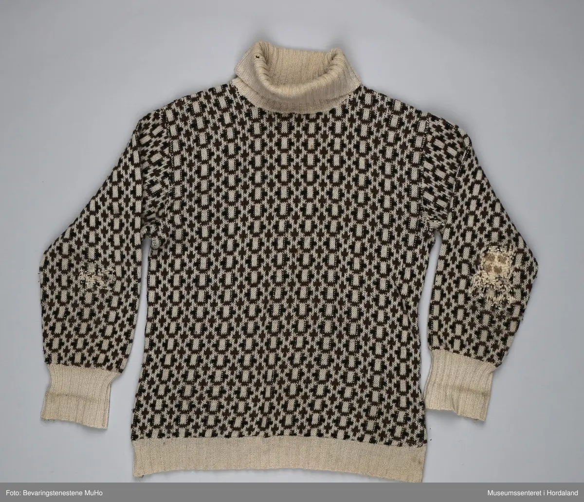 Krone ullgenser/islender med høg hals, str. 50. Vrangborder i beige, elles heildekkande mønster i beige, brun og svart. Genseren er godt brukt, og er stoppa på begge albogane og under armane.