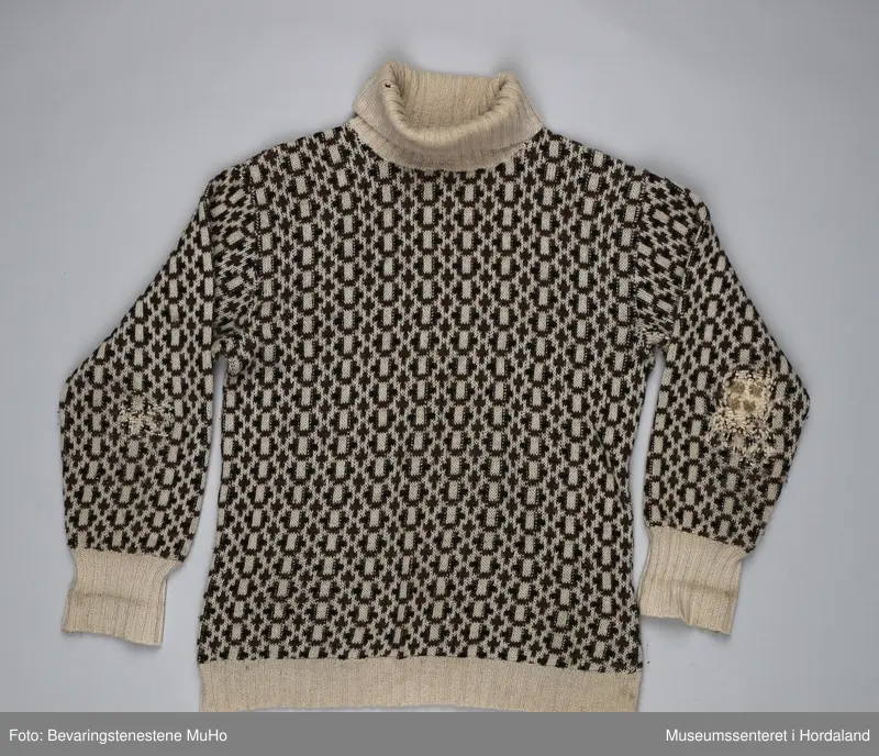 Krone ullgenser/islender med høg hals, str. 50. Vrangborder i beige, elles heildekkande mønster i beige, brun og svart. Genseren er godt brukt, og er stoppa på begge albogane og under armane.