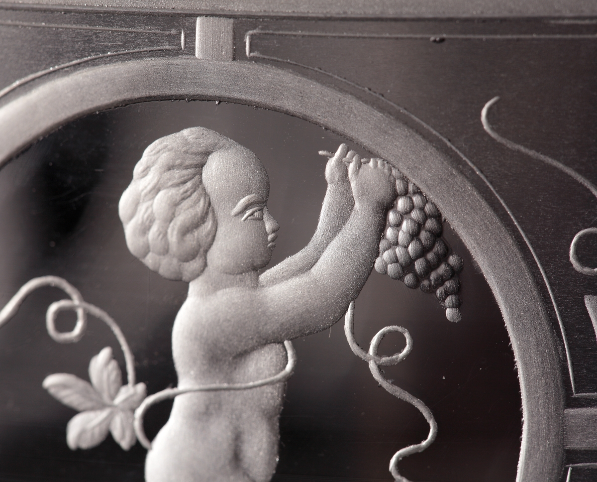 Skål eller urna med lock.
Skålen har en låg cylindrisk form som neråt smalnar av till en strut. Benet består av två ringar, och foten är trattformad. Locket är trattformat, där knoppen inleds med två ringar och slutligen en konisk knopp.
Skål och lock är mattsyrade i olika geometriska fält, vilka sedan graverats med organiska motiv. Skålen har runda fält vari åtta olika puttimotiv med bacchusinspiration graverats. På locket finns obearbetade "fönster", och på knoppen ett graverat draperi.