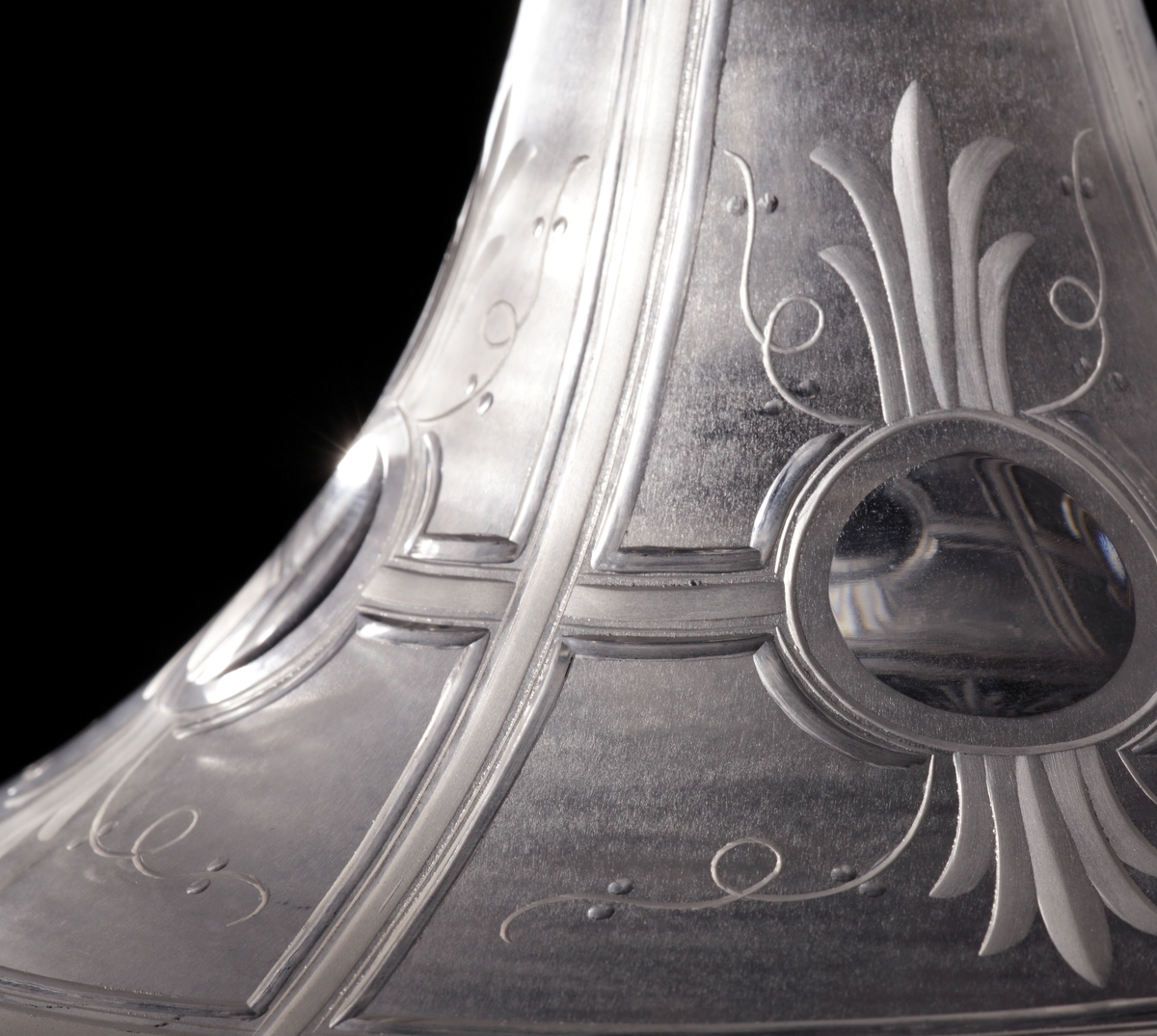 Skål eller urna med lock.
Skålen har en låg cylindrisk form som neråt smalnar av till en strut. Benet består av två ringar, och foten är trattformad. Locket är trattformat, där knoppen inleds med två ringar och slutligen en konisk knopp.
Skål och lock är mattsyrade i olika geometriska fält, vilka sedan graverats med organiska motiv. Skålen har runda fält vari åtta olika puttimotiv med bacchusinspiration graverats. På locket finns obearbetade "fönster", och på knoppen ett graverat draperi.