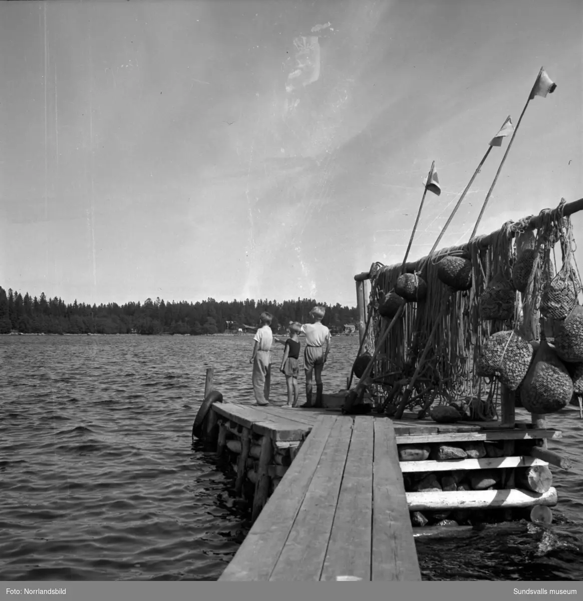 Barn på en fiskebrygga någonstans på Alnö. På bryggan hänger diverse rep och flytdon av kork.