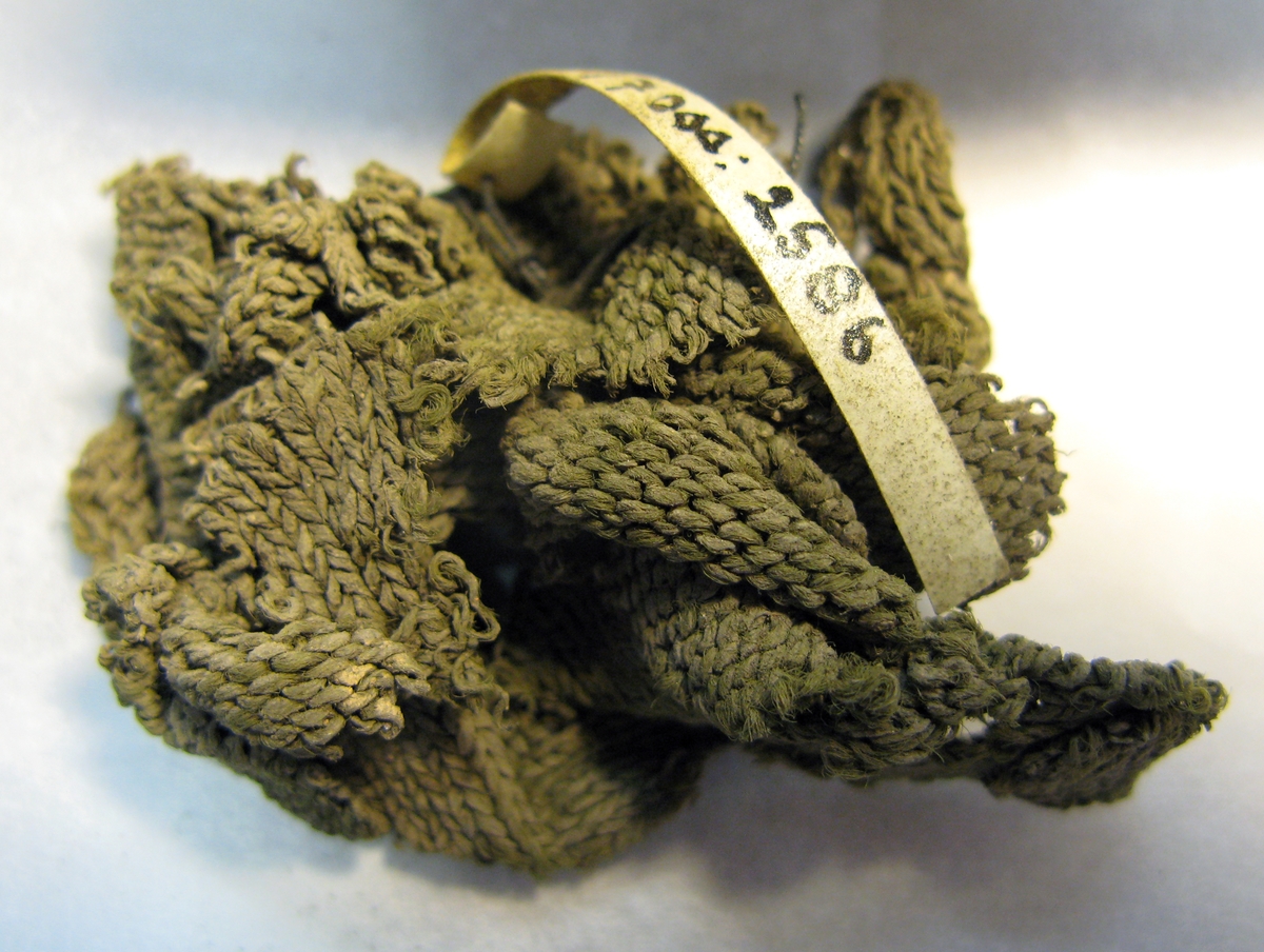 Flertalet mindre grågröna stickade fragment eventuellt av siden, stickade i slätstickning. Tråd samt mask och varvtäthet: 2-trådigt Z-spunnet, S-tvinnat masktäthet: 4-6 maskor/cm varvtäthet: 5-7 varv/cm.