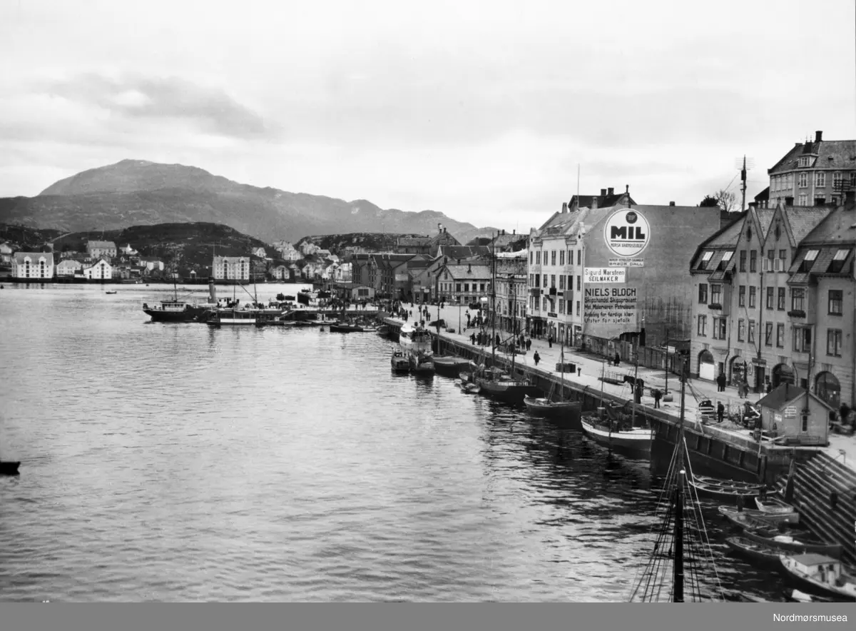 Kristiansund: Innlandet bak. Kirklandet: Piren, dampskip, rutebåter, Vågekaia, Børstrappa. Johnsenhuken. Skilt: Sigurd Marsteen, seilmaker. Niels Bloch, skipshandel. Foto: Georg Sverdrup nr 15, ca 1920. Samlingen har tillhørt Gert Faye-Gunnerud hvis mor var fra Walther-slekten i Kristiansund. Giver av samlingen er Tore Kristiansen. Fra Nordmøre museums fotosamlinger.