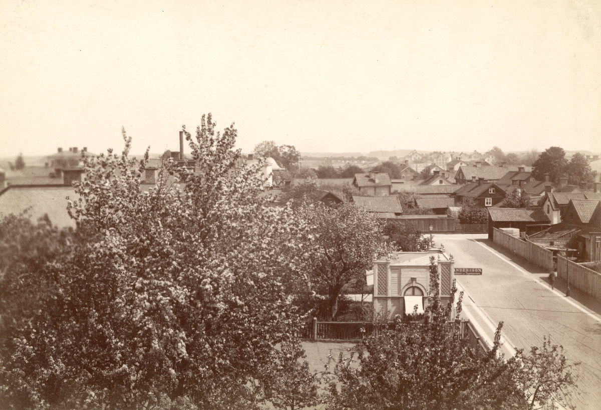 Vy mot Badhusgatan, dåvarande Biskopsgatan, österut. Tiden är omkring år 1890. I bildens förgrund ses delar av Grand hotells trädgård. Skylten på paviljongen visar vägen till Albert Fredrik Anderssons sadelmakeri. Byggnaden har tidigare förmodats ingått i Grands trädgård och fungerat som serveringspaviljong. Ny forskning visar att paviljongen istället uppfördes 1874 som fotoateljé för linköpingsfotografen Svante Leonard Rydholm. Upplysningsvis flyttades huset till friluftsmuseet Gamla Linköping 1958 för att där fungera som försäljningsställe. I bildens mellangrund ses trähusbebyggelsen inom kvarteret Bokbindaren.