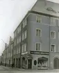 Svagt kollorerad vy mot Nygatan 42 i Linköping. Vid tiden drev Svenska Smöraffären butik i gatuplanet. Huset bortom är det så kallade Borgarhemmet. Uppfört 1912-13 med Linköpings fabriks och hantverksförening som byggherre.