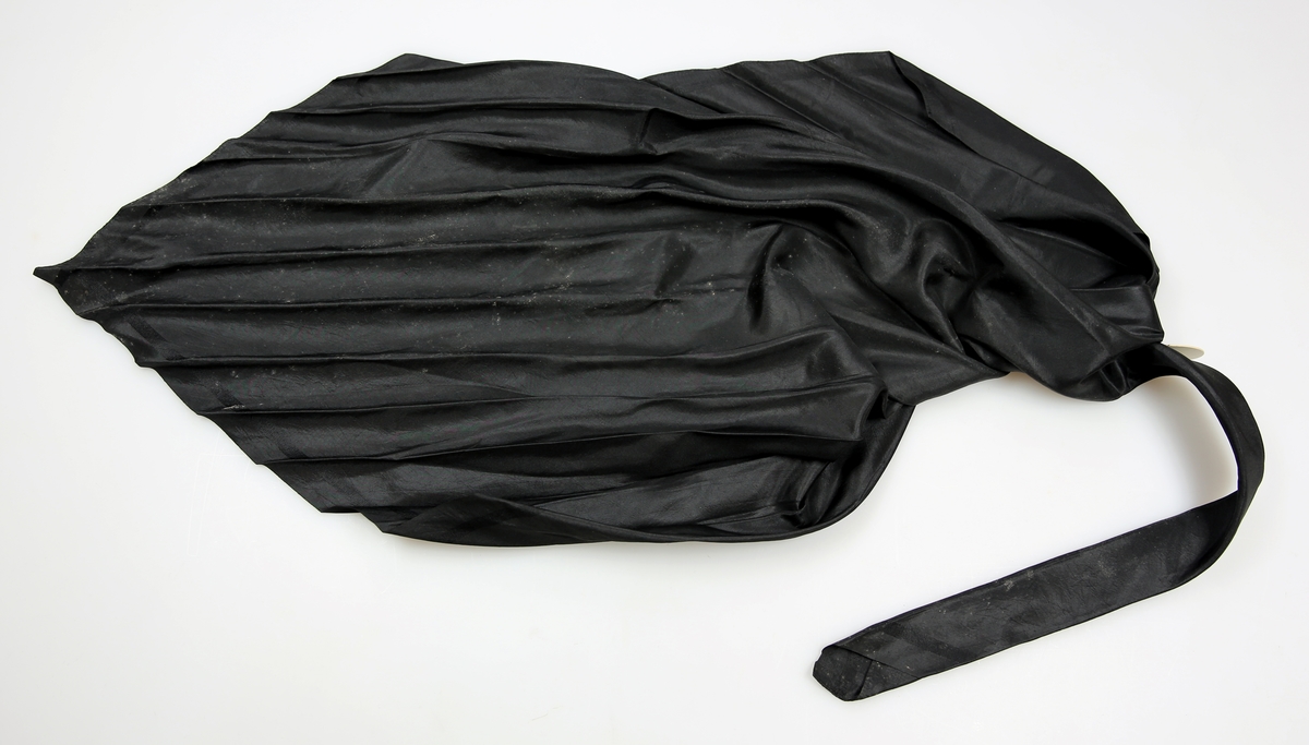 Svart, litt stivt silketørkle brettet som halstørkle. Full vevbredde. Faldet inn for hånd på to kanter.