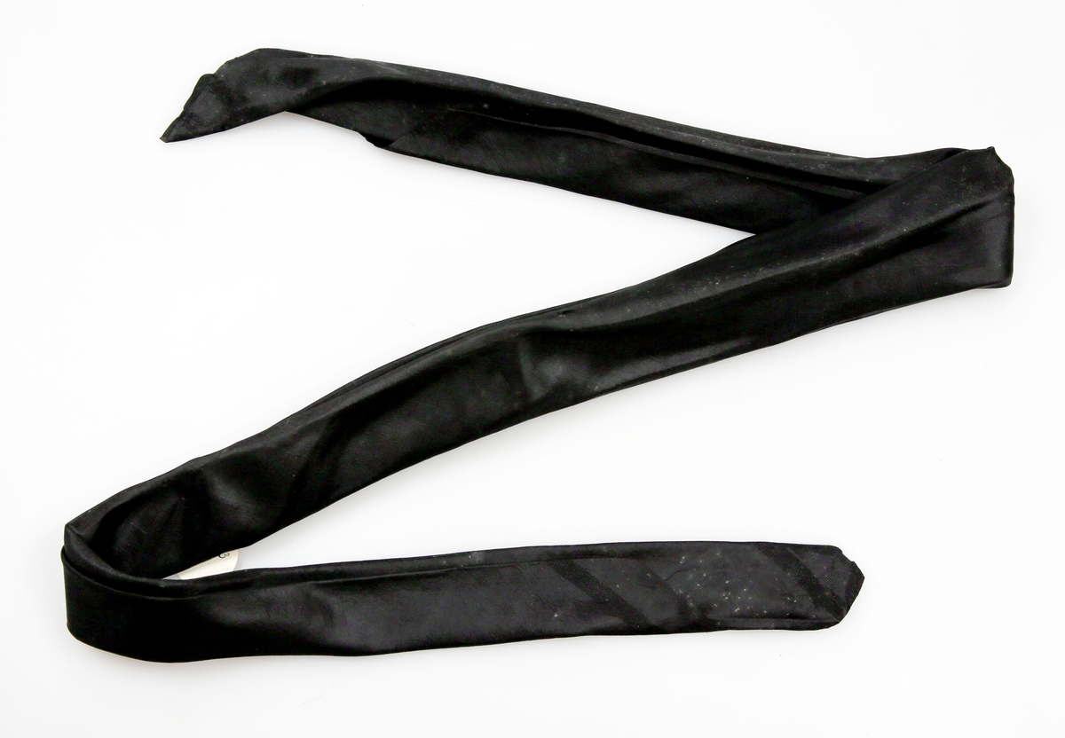 Svart, litt stivt silketørkle brettet som halstørkle. Full vevbredde. Faldet inn for hånd på to kanter.