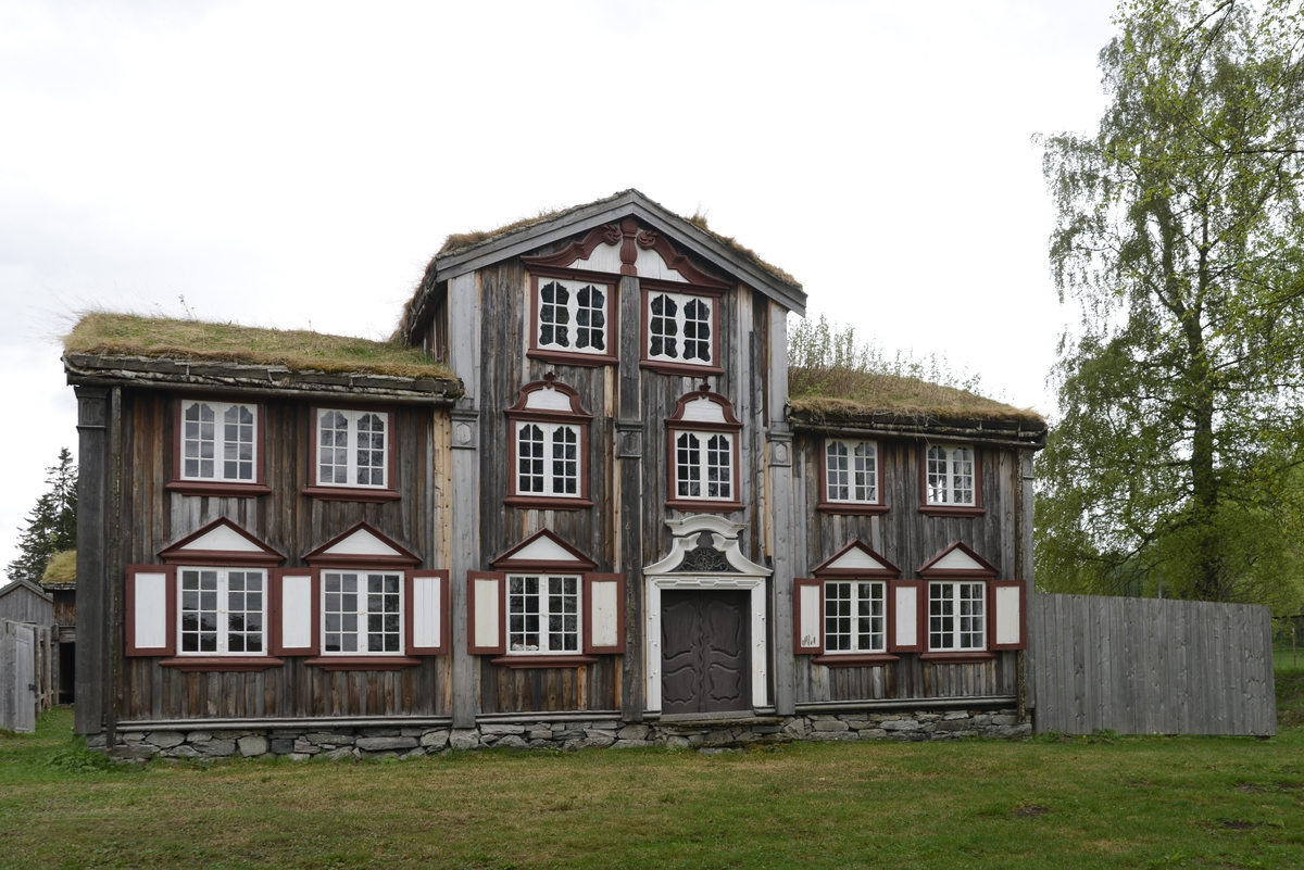 Bergmannsbolig av tømmer. Kledd med tømmermannspanel på gatefasaden. Taket er tekt med never og torv. Fasadeutstyret mot det offentlige rom holder en veldig høy standard. Bygningen er satt sammen av flere (to) eldre bolighus. Den tverrstilte midtarken er sekundært plassert oppå de sammenstilte bygningskroppene. Boligen fra Aspåsgården er sannsynligvis påbegynt  tidlig på 1700-tallet. Senere utvidet og mye forandret. Blant annet er det påbygd to omfar i hele 2. etg. og det er også satt inn større vinduskarmer. Trolig er dette skjedd i siste del av 1800-tallet. Det er gjenbrukt bygningselementer fra et sosialt høyere sjikt. Bygningen har to rom med fyllingspanelte vegger. - Et  rom i 2. etg. og et i midtarken. Disse to rommene har fått sine nytilvirkede veggpaneler etter at de har fått nåværende romhøyde og etter at det er satt inn større vinduskarmer. Bygningen er endret helt inn mot 1900-tallet.  Pløyd panel, brukt i bislag mot bakgården, representerer et siste trinn i Rørosbebyggelsens utviklingshistorie. Sto på Flanderborg, Røros. Gjenreist på Sverresborg 1917. I forbindelse med oppføringa på museet har bygningen vært gjenstand for omfattende tilbakeføringsforsøk, med blant annet ens vindusrammer for hver etasje. Ikke noe av det gamle panelet på gatefasaden er gjenbrukt. Nytt panel har også fått en annen utbredelse og underdeling enn tidligere. På Røros var bl. a. også grundmuren dekt av panel. Alt tømmermannspanel er nytt fra 1917. Dagens utseende er eksteriørmessig utvilsomt museumsskapt. Endringene, som er gjennomført på museet, har bidratt til klart å svekke et veldig godt eksempel på folkelig, lokal byggeskikk. 