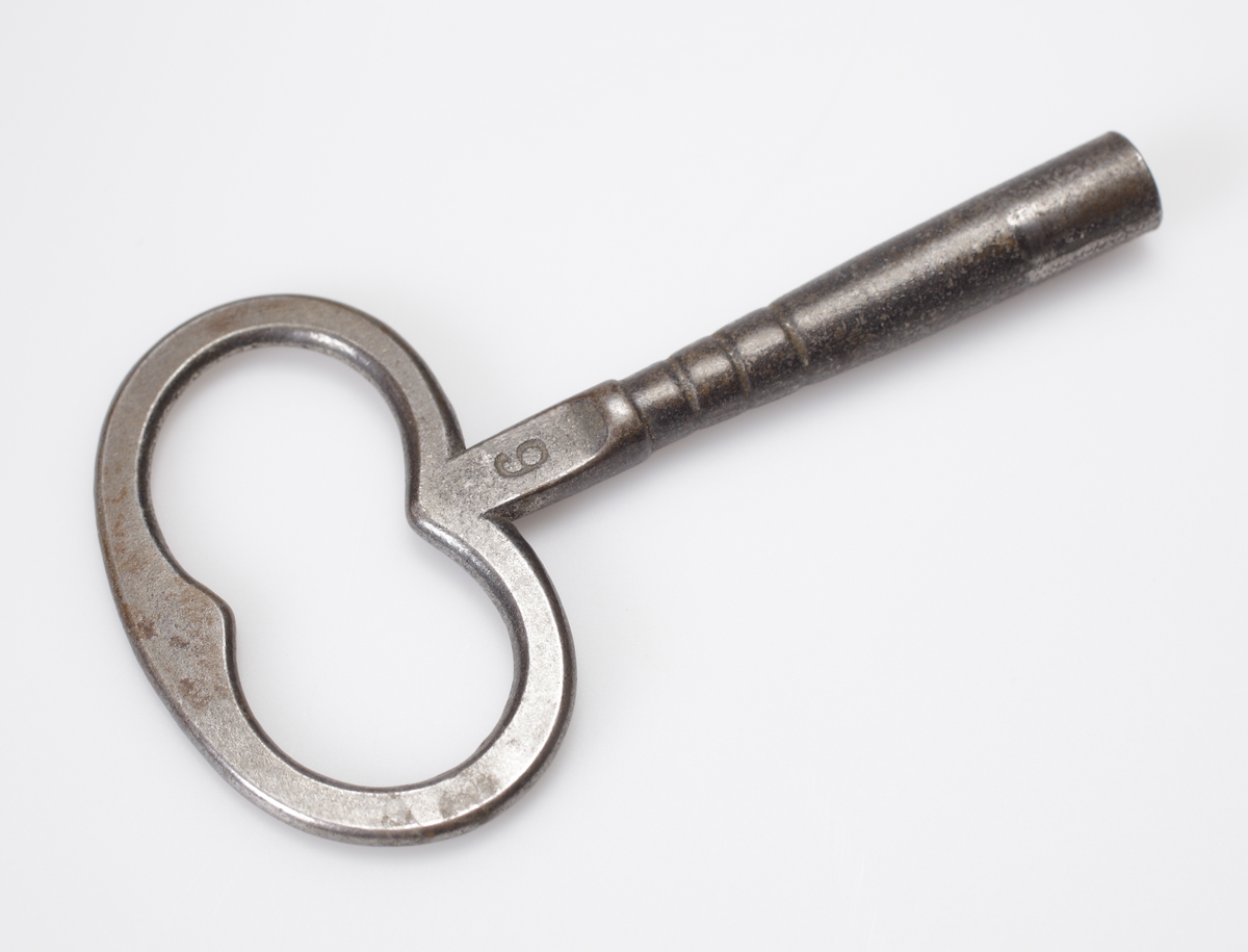 Bordspendyl / Bordsstudsare.
Vit emaljerad urtavla försedd med arabiska siffror i en rund, guldbronserad överdel av trä, som vilar på tre snidade delfiner. Högst upp en guldbronserad urna. 
Cylindrisk fot av trä, målad i rödbrun marmorimitation med guldbronserade partier. Tillhörande urnyckel av järn.