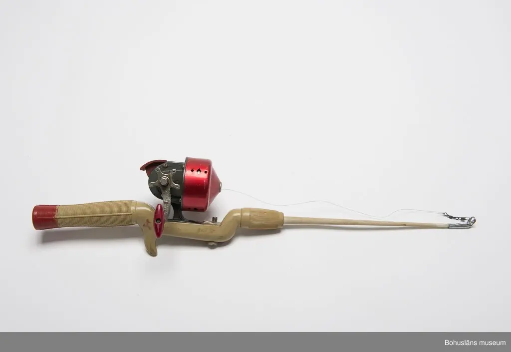 Spö av grön-grått konstmaterial. Rött längst bak på handtaget.
Inpressad text: "RECORD". I spöspetsen är det en metallhylsa med en
en ring som linan skall löpa genom.
Röd och grå inkapslad haspelrulle med vevhandtag. Märke: "BELLY No. 58".