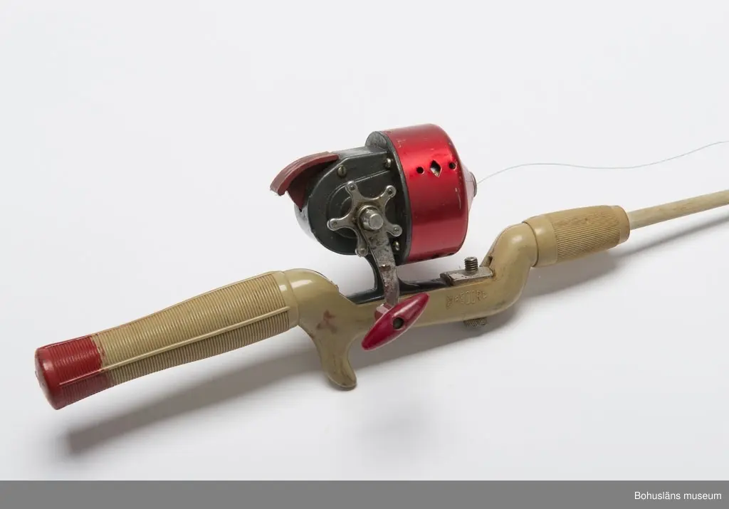 Spö av grön-grått konstmaterial. Rött längst bak på handtaget.
Inpressad text: "RECORD". I spöspetsen är det en metallhylsa med en
en ring som linan skall löpa genom.
Röd och grå inkapslad haspelrulle med vevhandtag. Märke: "BELLY No. 58".