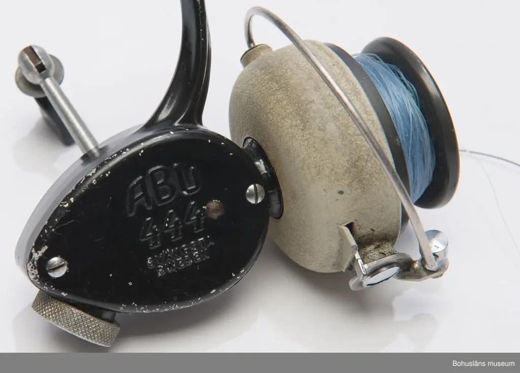 Svart haspelrulle med grått spolhus. Ledbart vevhandtag. Text på gavelplattan: "ABU 444 SVÄNGSTA SWEDEN". Blå lina av polyamidfiber En extra rulle i en röd cylindrisk ask av konstmaterial (H 2,5 Di 6,5 cm). Märkt "ABU SVÄNGSTA SWEDEN".
En behållare i konstmaterial med rullolja, den har rött lock samt samt text på kroppen "ABU SVÄNGSTA SWEDEN" (H 6,3 Di 1,2 cm) . En
broschyr "HANDBOK I HASPEL FISKE" (L 14,8 H 11,3 cm) med instruktioner om skötsel och användning av rullen. Samtliga föremål låg ursprungligen i en fyrkantig låda av papp (L 14 H 12 B 9 cm). Lådan är svart, gul och vit. Text bl a "ABU 444". Lådan är mycket lagad med tejp.
Tillhör fiskespö i fodral UM024251. Har även använts på UM023750.
*Tidigare sakord: Fiskerulle i originallåda.