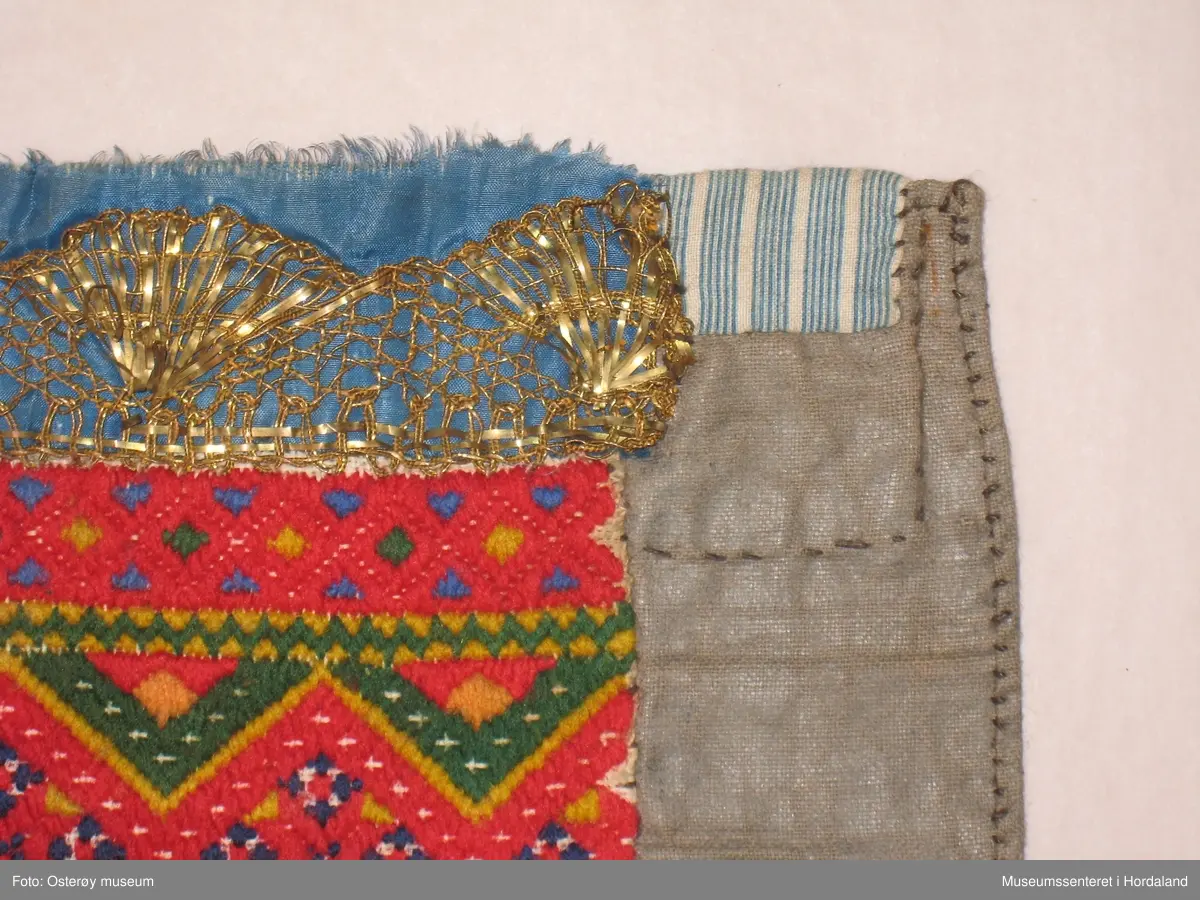 Brodert med ullgarn i plattsaum. Alt er handlaga. Hovudmotiv er små åttebladroser i border. Oppe er det påsydd eit blått silkeband med eit breitt gullband (i forgylt sølvtråd) utanpå silkebandet. Alt er montert på eit tynt, vokset bomullslerret. Oppe på baksida er det eit ekstra bomullstoff (blåstripet). Bokstavane BODM er broderte inn nede på bringeduken i kross-sting.